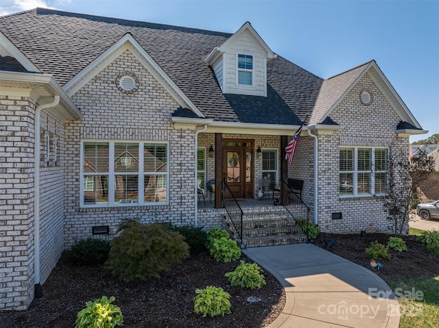 view of front of property with crawl space, a porch, a shingled roof, and brick siding