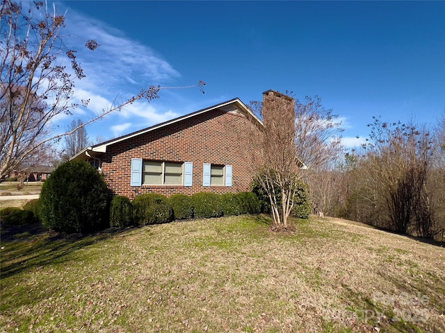 view of home's exterior with a yard, a chimney, and brick siding