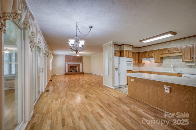 kitchen with light wood finished floors, white appliances, light countertops, a textured ceiling, and under cabinet range hood