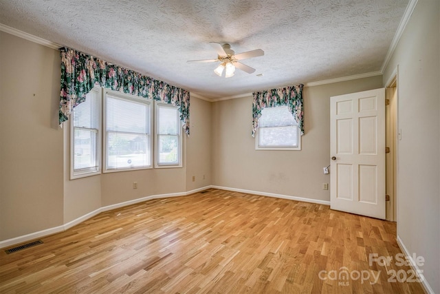 spare room with crown molding, a ceiling fan, visible vents, and light wood-style flooring