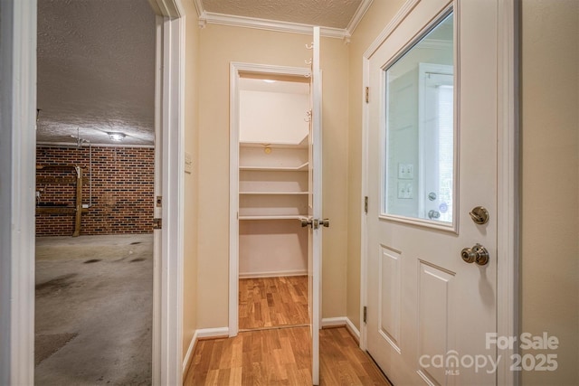 interior space with a textured ceiling, ornamental molding, light wood-style flooring, and brick wall