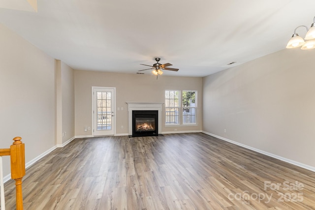 unfurnished living room with a fireplace with flush hearth, baseboards, wood finished floors, and ceiling fan with notable chandelier