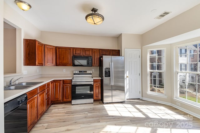 kitchen featuring visible vents, light wood-style flooring, light countertops, black appliances, and a sink