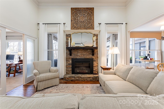 living room featuring a stone fireplace, a healthy amount of sunlight, wood finished floors, and crown molding