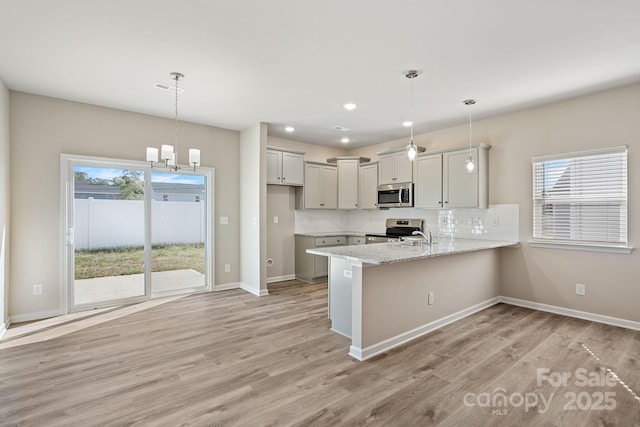 kitchen featuring tasteful backsplash, light wood-type flooring, appliances with stainless steel finishes, kitchen peninsula, and pendant lighting