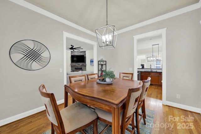 dining area with crown molding, baseboards, ceiling fan with notable chandelier, a fireplace, and light wood finished floors