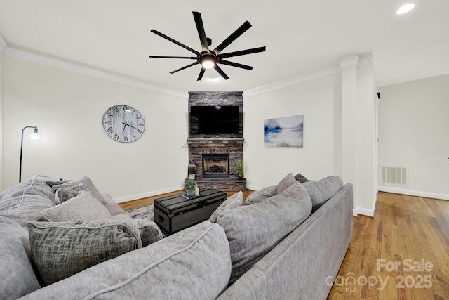 living room with crown molding, a stone fireplace, baseboards, visible vents, and light wood finished floors