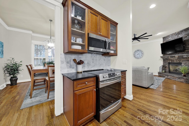 kitchen with glass insert cabinets, crown molding, stainless steel appliances, dark countertops, and brown cabinetry