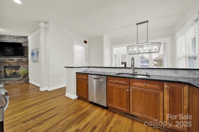 kitchen featuring stainless steel dishwasher, hanging light fixtures, a sink, brown cabinets, and a fireplace