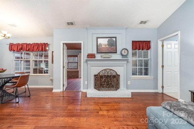 living area featuring a brick fireplace, wood finished floors, visible vents, and baseboards