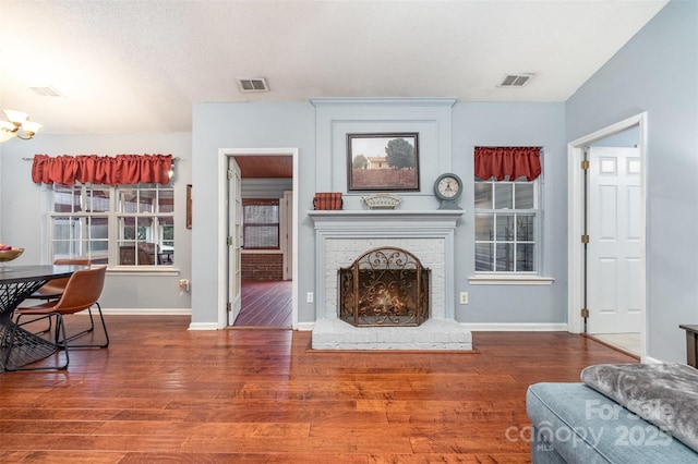 living room with visible vents, a brick fireplace, baseboards, and wood finished floors