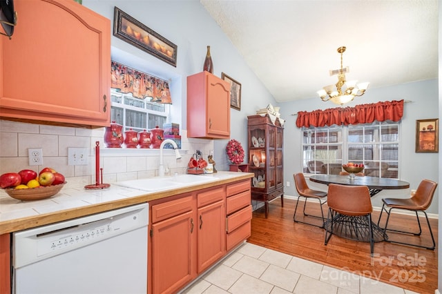 kitchen featuring a sink, backsplash, white dishwasher, a chandelier, and tile counters