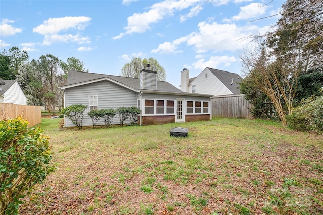 rear view of property with a chimney, a sunroom, a yard, and fence