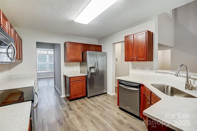 kitchen featuring appliances with stainless steel finishes, light countertops, a textured ceiling, light wood-type flooring, and a sink