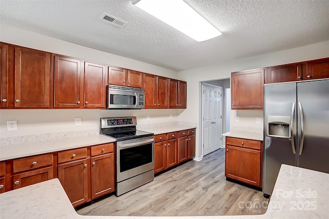 kitchen featuring stainless steel appliances, light countertops, visible vents, light wood-style floors, and a textured ceiling