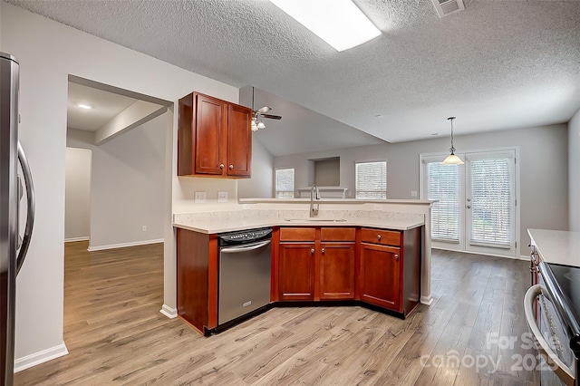 kitchen featuring decorative light fixtures, stainless steel appliances, light countertops, a sink, and light wood-type flooring