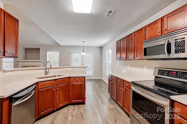 kitchen featuring decorative light fixtures, light wood finished floors, light countertops, appliances with stainless steel finishes, and a sink