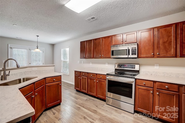 kitchen with stainless steel appliances, a sink, visible vents, light wood finished floors, and decorative light fixtures