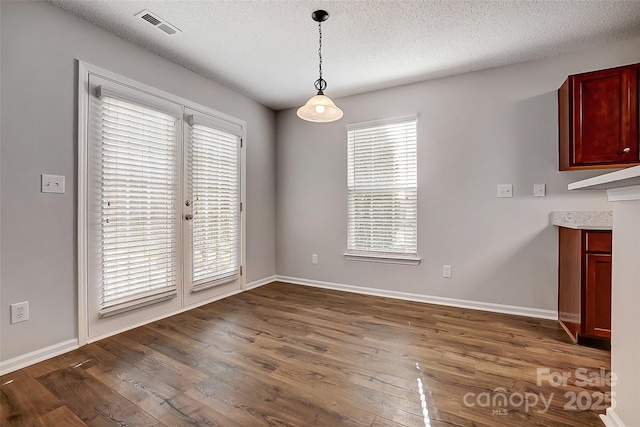 unfurnished dining area with baseboards, visible vents, dark wood finished floors, and a textured ceiling