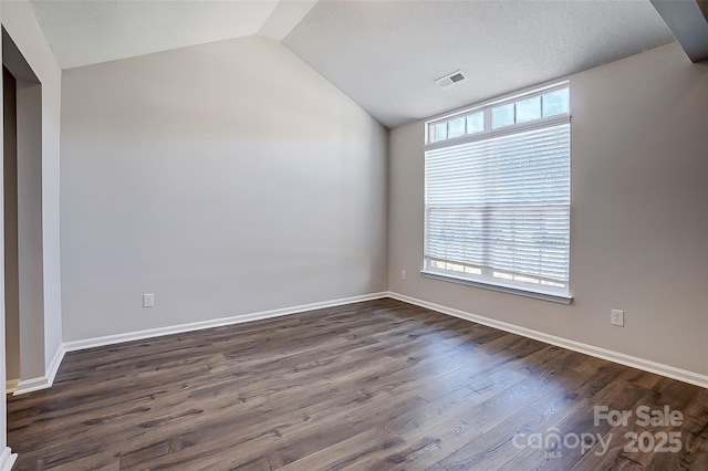 spare room featuring lofted ceiling, dark wood-style flooring, visible vents, and baseboards