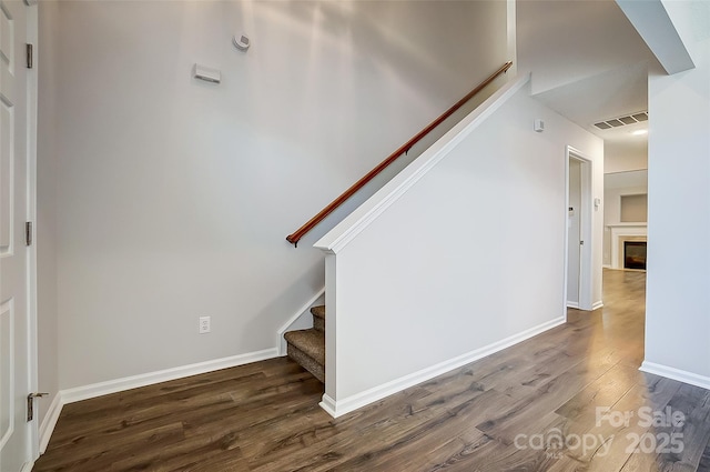 stairway featuring a glass covered fireplace, wood finished floors, visible vents, and baseboards