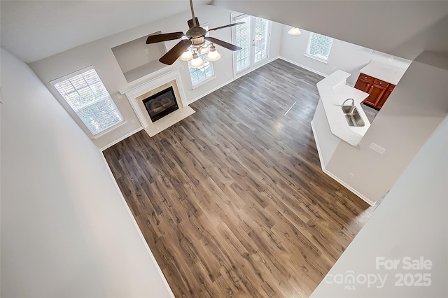 unfurnished living room with dark wood finished floors, ceiling fan, vaulted ceiling, a fireplace, and a sink