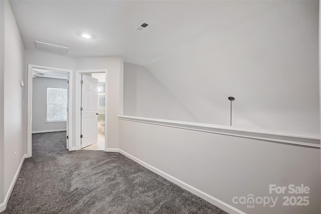 corridor with vaulted ceiling, dark carpet, visible vents, and baseboards