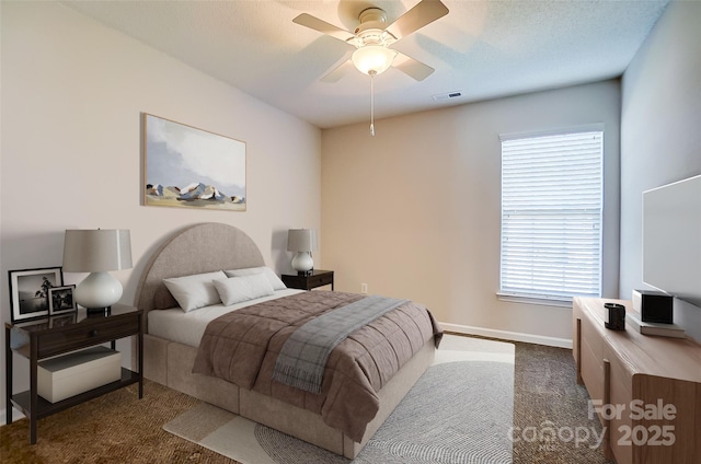 bedroom with ceiling fan, a textured ceiling, visible vents, baseboards, and dark carpet