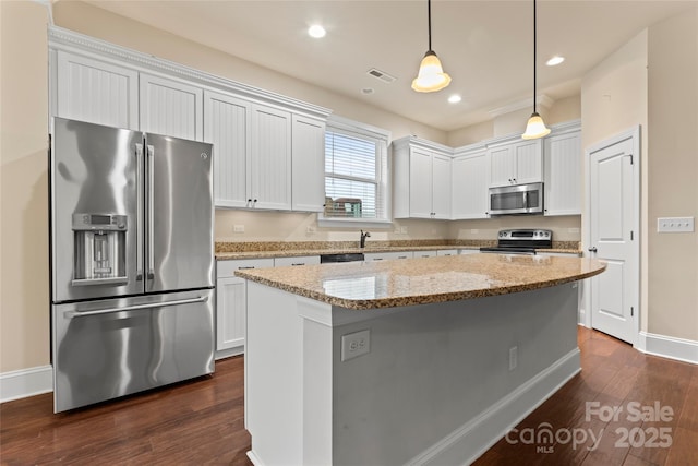 kitchen featuring appliances with stainless steel finishes, white cabinets, light stone counters, and decorative light fixtures