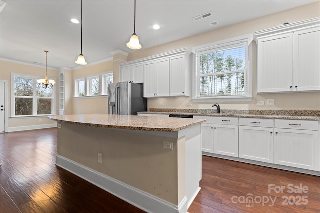 kitchen featuring high end fridge, hanging light fixtures, white cabinetry, light stone counters, and a kitchen island