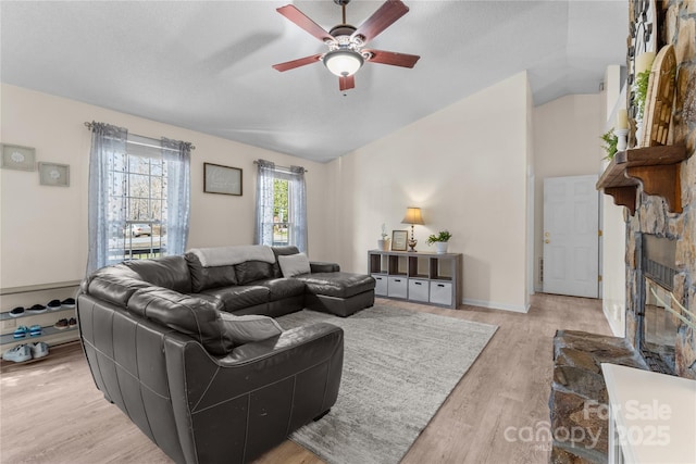 living room featuring a fireplace, light hardwood / wood-style floors, ceiling fan, and vaulted ceiling