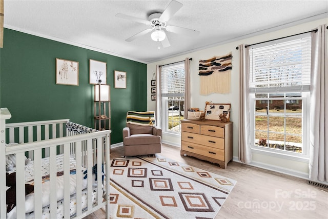 bedroom with ceiling fan, wood-type flooring, a textured ceiling, and a crib