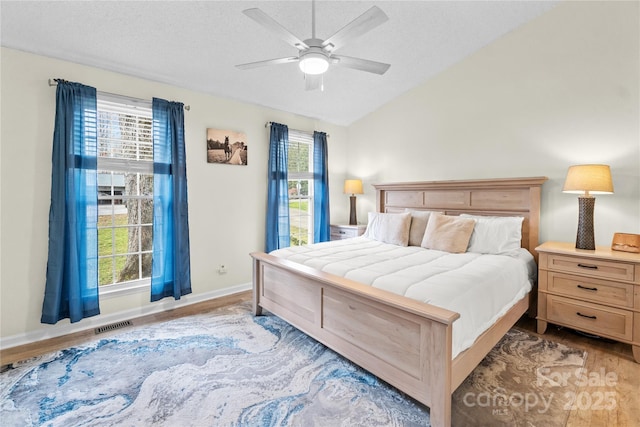 bedroom with lofted ceiling, a textured ceiling, multiple windows, and light hardwood / wood-style flooring