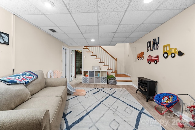 living room with hardwood / wood-style flooring, a paneled ceiling, and a wood stove