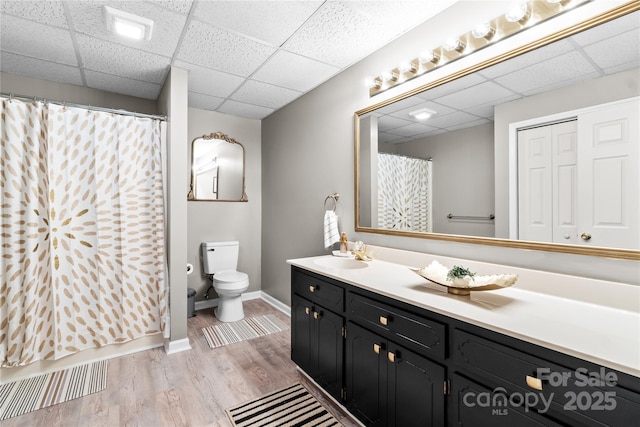 bathroom with toilet, a shower with curtain, vanity, hardwood / wood-style flooring, and a drop ceiling