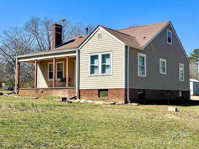 back of house with covered porch, a lawn, and a chimney