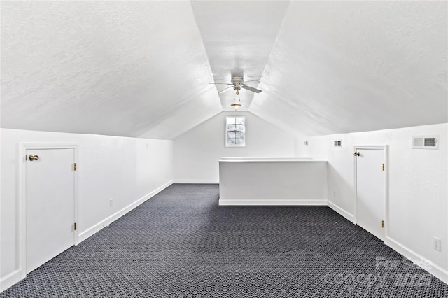 bonus room featuring dark colored carpet, vaulted ceiling, ceiling fan, and a textured ceiling