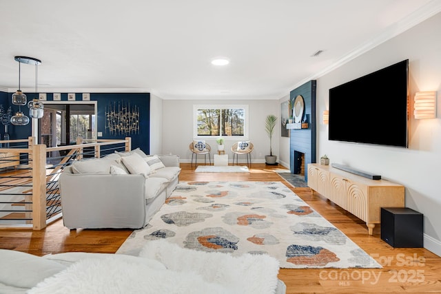 living area featuring baseboards, visible vents, ornamental molding, wood finished floors, and a fireplace