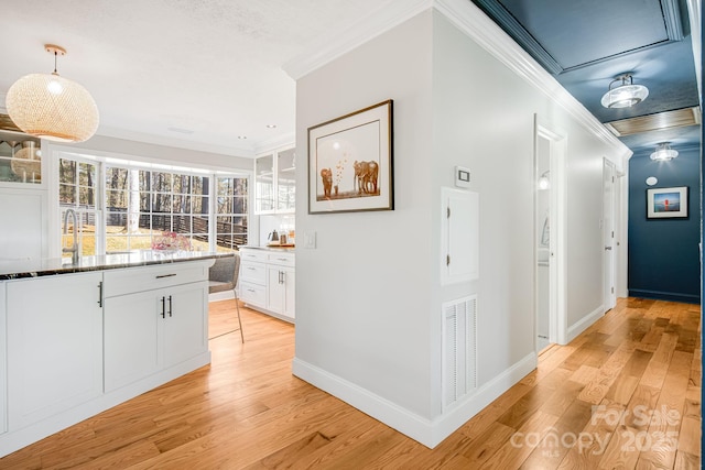 hallway featuring light wood-type flooring, visible vents, crown molding, and baseboards