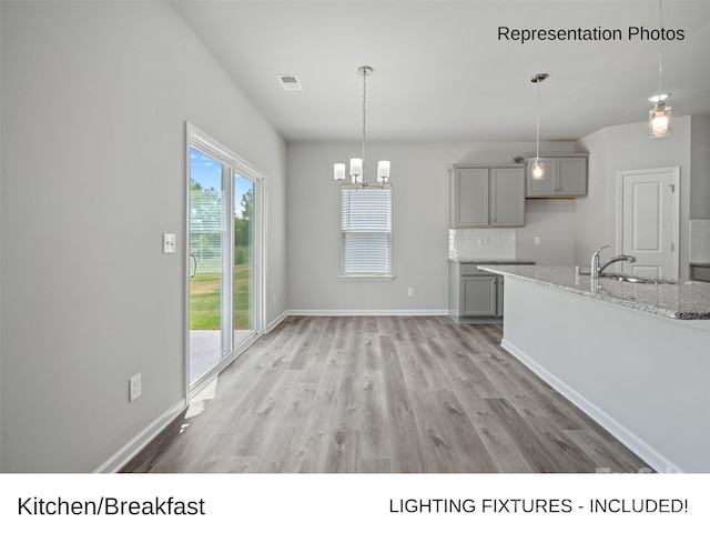 kitchen with sink, gray cabinets, tasteful backsplash, light stone countertops, and decorative light fixtures