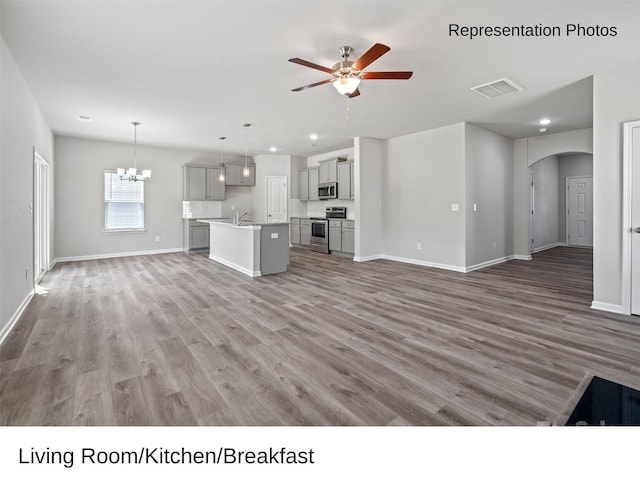 unfurnished living room featuring hardwood / wood-style flooring, sink, and ceiling fan with notable chandelier