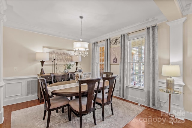 dining area with wainscoting, ornamental molding, wood finished floors, ornate columns, and a notable chandelier