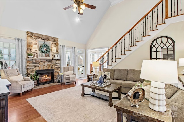 living room featuring high vaulted ceiling, a fireplace, wood finished floors, a ceiling fan, and stairway