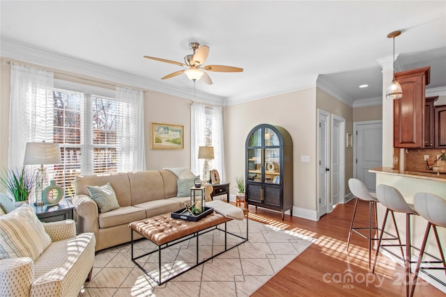 living area featuring baseboards, crown molding, light wood finished floors, and ceiling fan