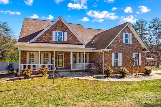 view of front of house featuring a porch, a front yard, brick siding, and a shingled roof