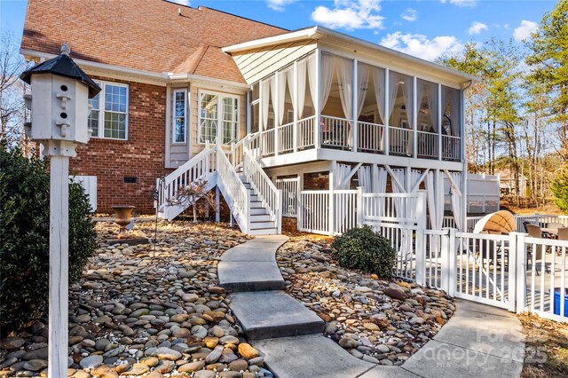 view of front of home featuring brick siding, fence, a sunroom, stairs, and roof with shingles