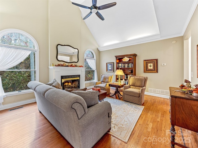 living room with ornamental molding, plenty of natural light, high vaulted ceiling, and light hardwood / wood-style flooring