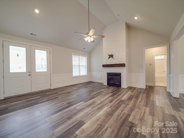 unfurnished living room with ceiling fan, high vaulted ceiling, a large fireplace, dark hardwood / wood-style flooring, and french doors