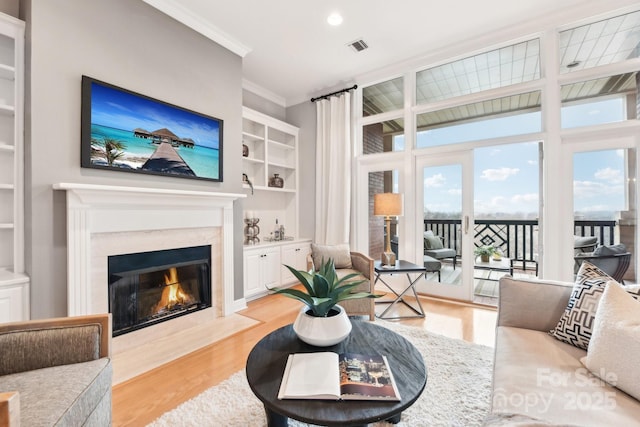 living room with crown molding, built in features, a high end fireplace, and light hardwood / wood-style flooring