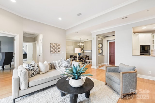 living room featuring a notable chandelier, ornamental molding, and light wood-type flooring